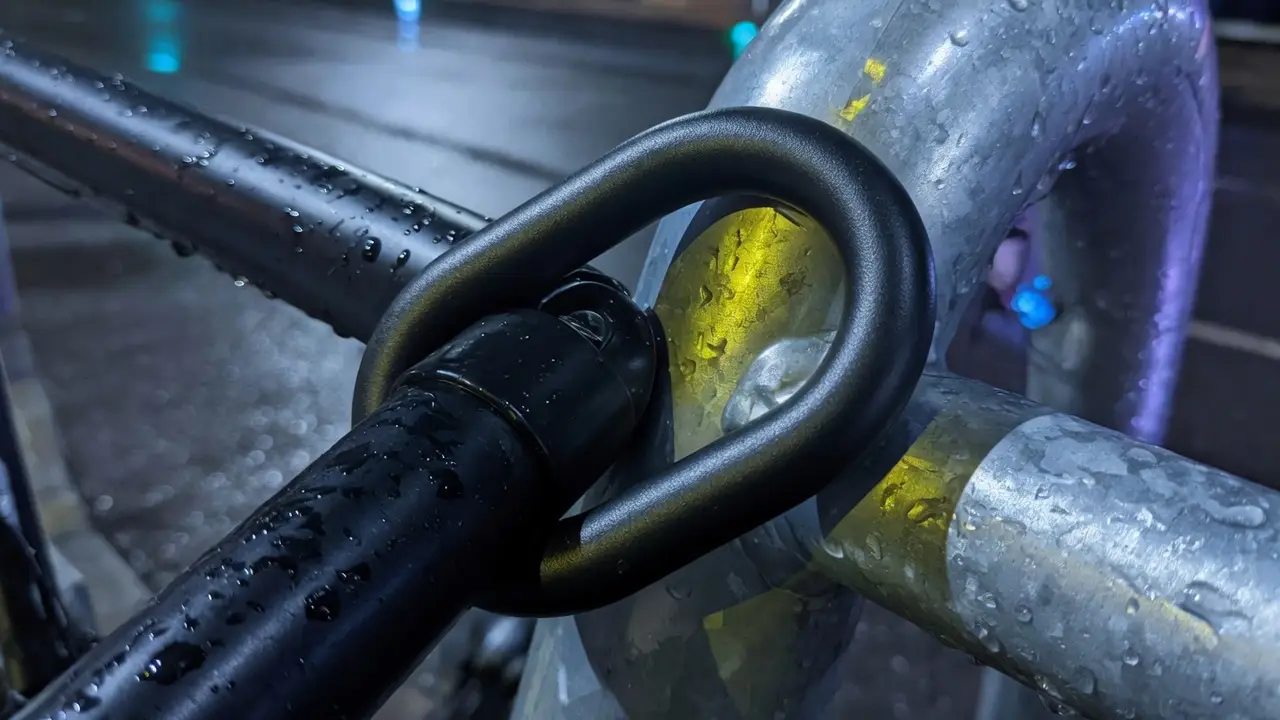 A lock closing around a galvanised stand and a frame tube in the rain. Editorial photograph.